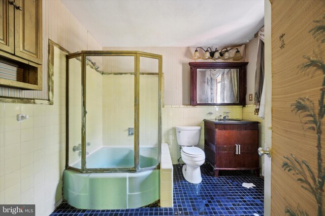 full bathroom with combined bath / shower with glass door, toilet, tile walls, vanity, and tile patterned flooring