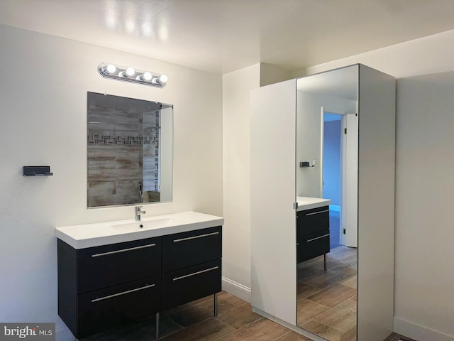 bathroom featuring baseboards, wood finish floors, tiled shower, and vanity