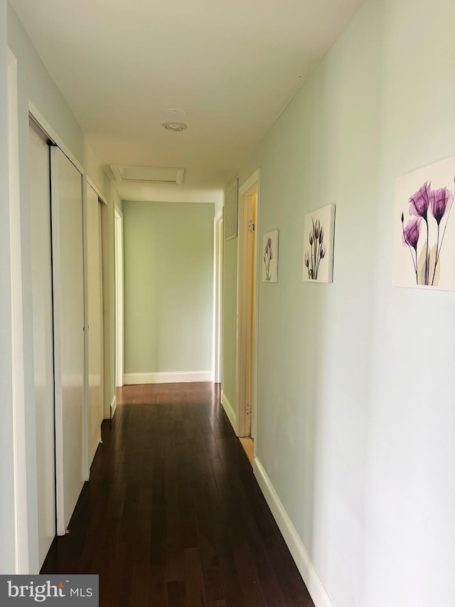 hallway with dark wood-type flooring, attic access, and baseboards