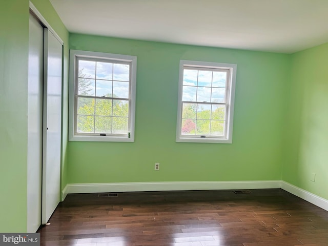 empty room featuring dark wood-type flooring, baseboards, and visible vents