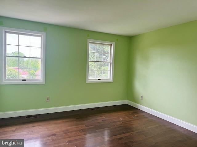 unfurnished room with dark wood-style flooring, baseboards, and visible vents