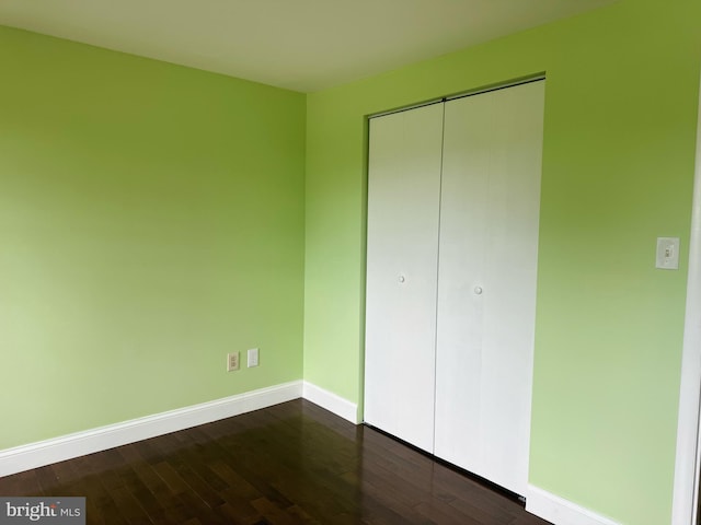 unfurnished bedroom with baseboards, dark wood-type flooring, and a closet