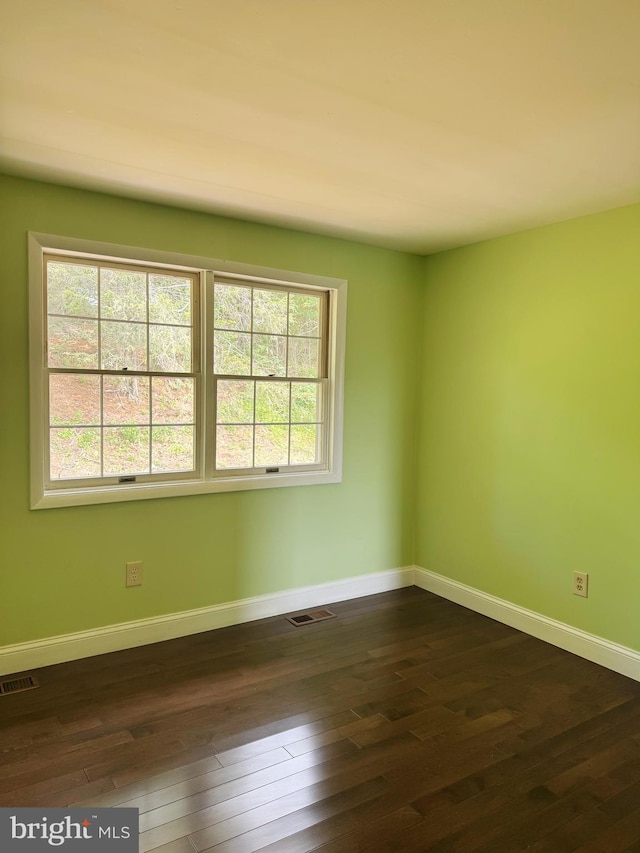 empty room with baseboards, visible vents, and dark wood finished floors