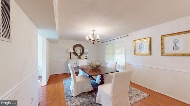 dining room with wood-type flooring, an inviting chandelier, and ornamental molding