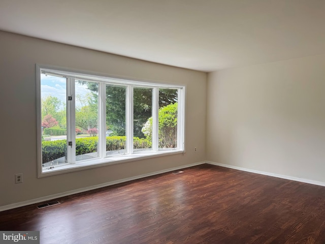 unfurnished room featuring baseboards, visible vents, and dark wood-type flooring