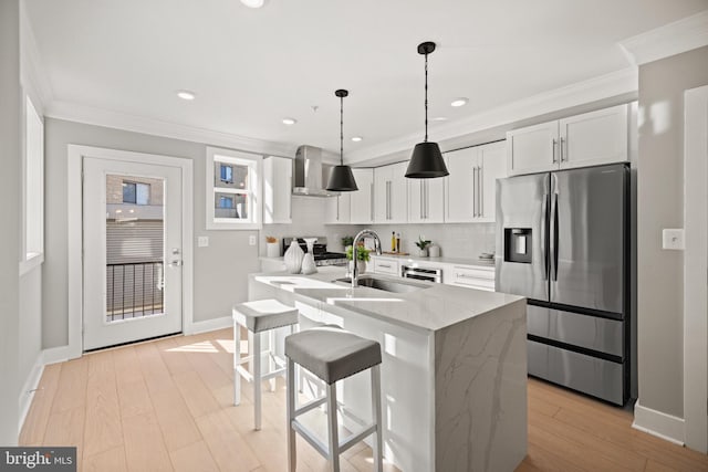 kitchen featuring wall chimney range hood, light stone countertops, white cabinetry, appliances with stainless steel finishes, and light hardwood / wood-style floors