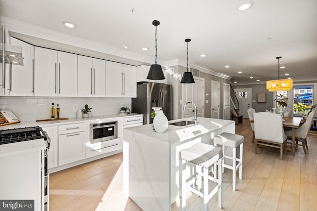 kitchen with decorative light fixtures, white cabinets, stainless steel appliances, and an island with sink