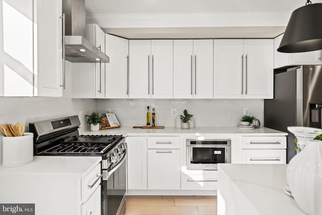 kitchen featuring wall chimney exhaust hood, white cabinetry, appliances with stainless steel finishes, light stone counters, and tasteful backsplash