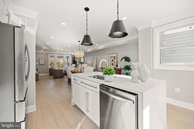 kitchen with white cabinets, hanging light fixtures, appliances with stainless steel finishes, a kitchen island with sink, and light hardwood / wood-style floors