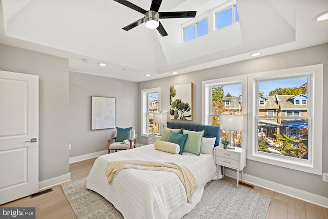 bedroom with ceiling fan, a tray ceiling, multiple windows, and light wood-type flooring