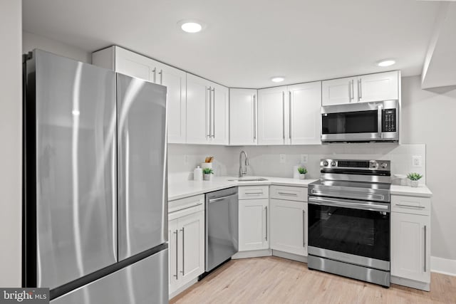 kitchen with appliances with stainless steel finishes, sink, light wood-type flooring, backsplash, and white cabinetry