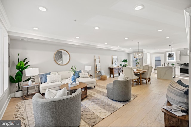 living room featuring an inviting chandelier, light hardwood / wood-style flooring, ornamental molding, and plenty of natural light