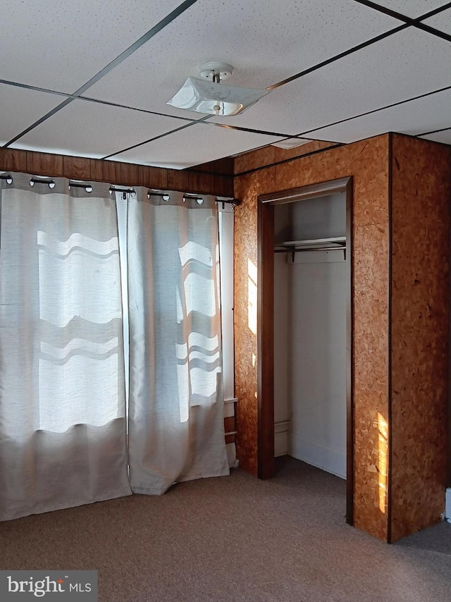 unfurnished bedroom featuring a drop ceiling, a closet, and carpet flooring