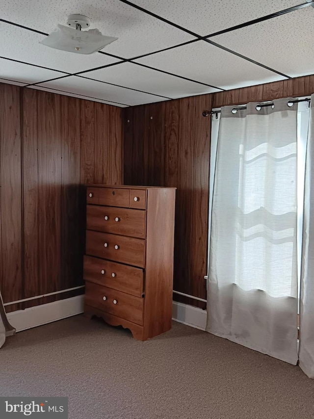 unfurnished bedroom featuring wooden walls, a drop ceiling, and carpet floors