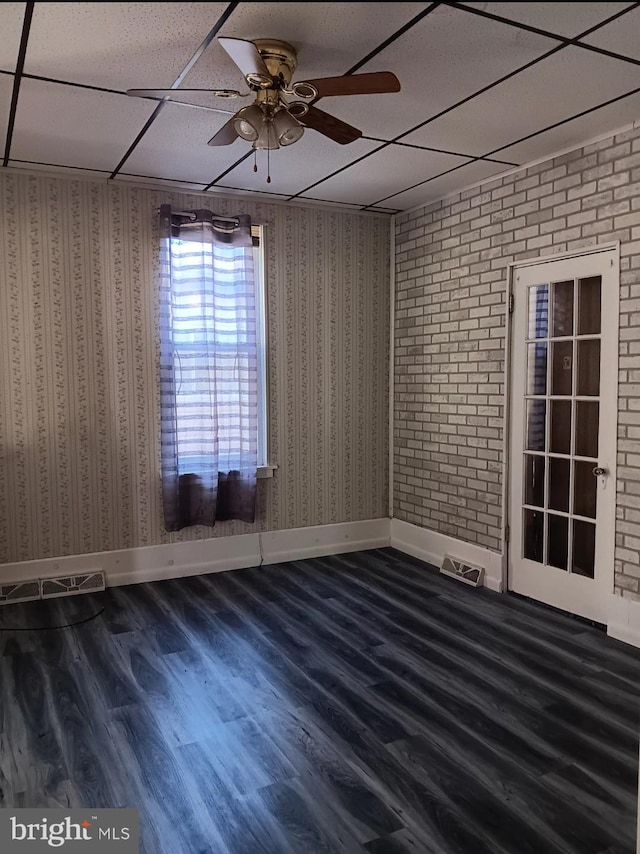 spare room with a paneled ceiling, ceiling fan, brick wall, and dark hardwood / wood-style flooring