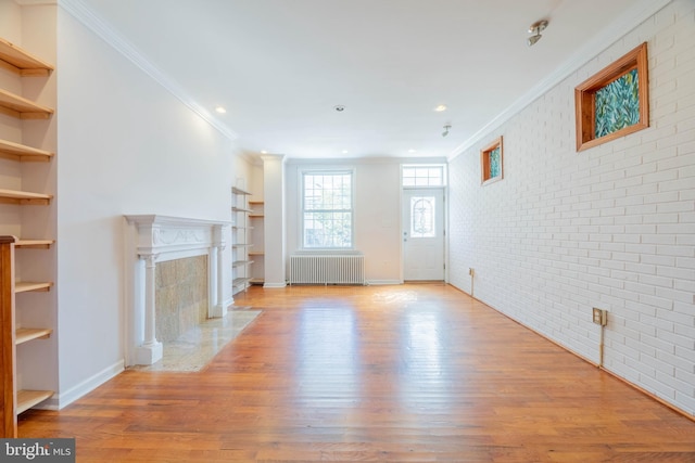 unfurnished living room with radiator heating unit, brick wall, crown molding, built in features, and light hardwood / wood-style flooring