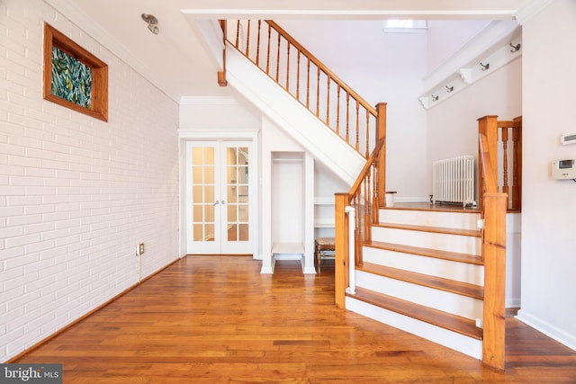 staircase featuring french doors, ornamental molding, brick wall, and hardwood / wood-style flooring