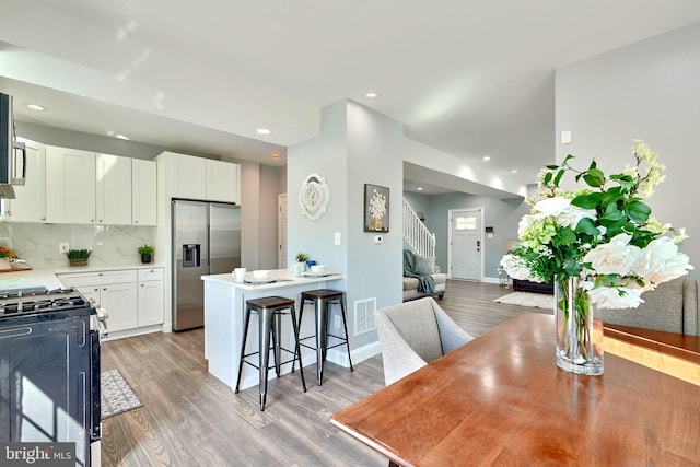 kitchen with a kitchen bar, range with gas cooktop, hardwood / wood-style flooring, white cabinets, and stainless steel fridge with ice dispenser