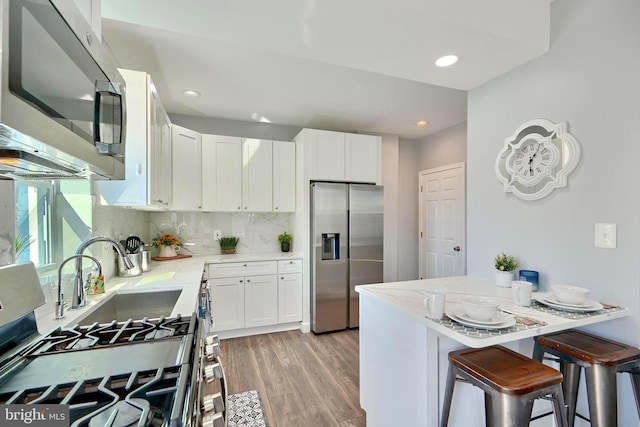 kitchen with white cabinets, stainless steel appliances, light stone counters, and light hardwood / wood-style flooring