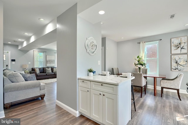 kitchen featuring white cabinets, a healthy amount of sunlight, light stone countertops, and hardwood / wood-style flooring