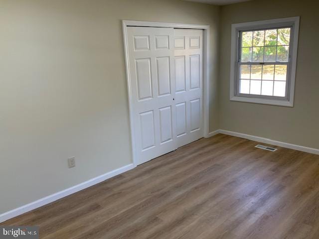 unfurnished bedroom with baseboards, a closet, visible vents, and wood finished floors