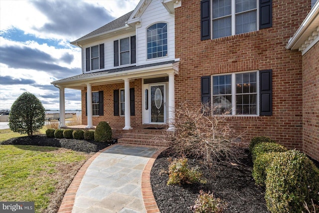 doorway to property with a porch and brick siding