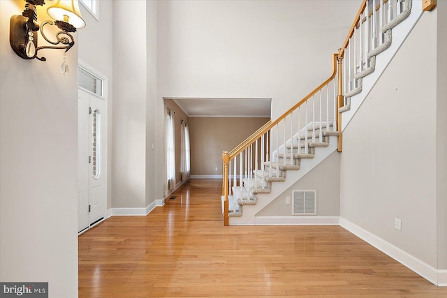 entrance foyer featuring hardwood / wood-style flooring, a towering ceiling, visible vents, stairs, and baseboards