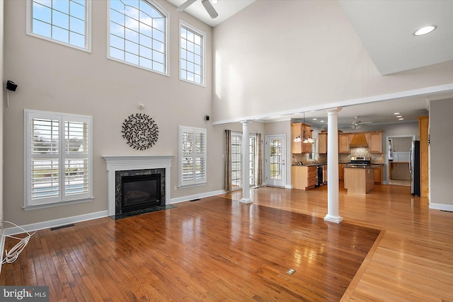 unfurnished living room featuring decorative columns, a fireplace, visible vents, a ceiling fan, and hardwood / wood-style flooring