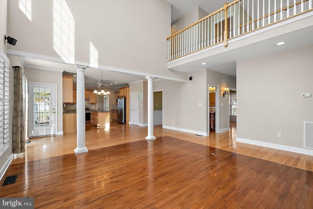 unfurnished living room featuring light wood-type flooring, visible vents, decorative columns, and baseboards