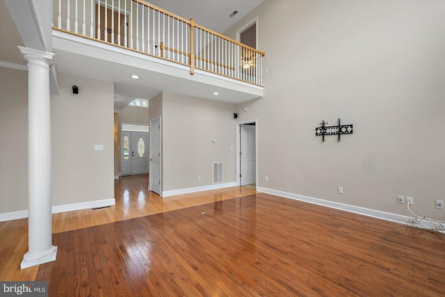 unfurnished living room featuring decorative columns, visible vents, hardwood / wood-style floors, a high ceiling, and baseboards