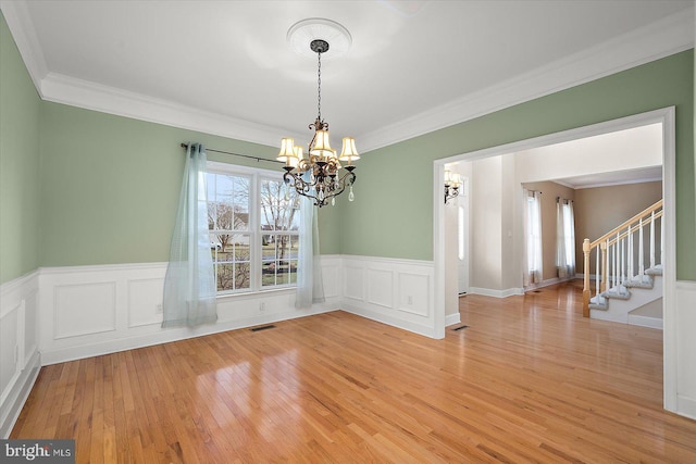 unfurnished dining area with crown molding, light wood finished floors, visible vents, stairway, and a chandelier