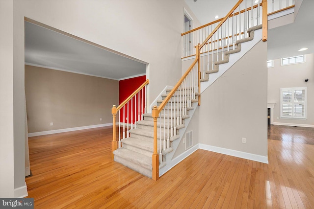 stairway with visible vents, baseboards, a towering ceiling, wood-type flooring, and a fireplace