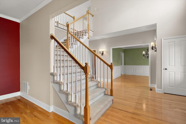 stairway with crown molding, visible vents, a high ceiling, wood finished floors, and baseboards