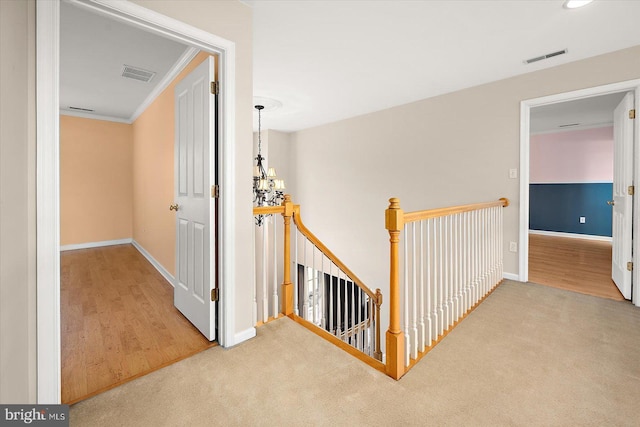 hall featuring carpet floors, visible vents, a notable chandelier, and an upstairs landing