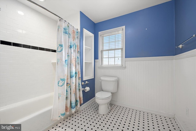 bathroom featuring a wainscoted wall, shower / bathtub combination with curtain, and toilet