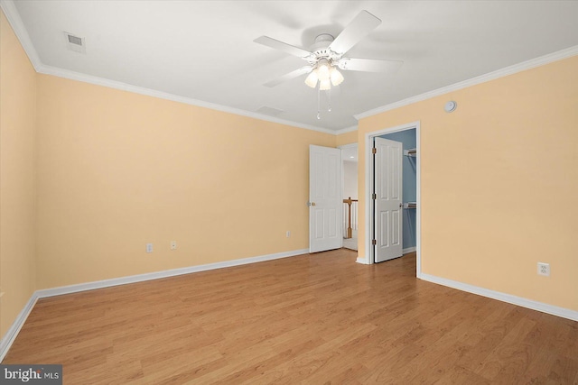 unfurnished bedroom with light wood-style floors, a walk in closet, crown molding, and baseboards