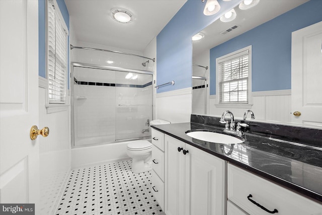 bathroom with visible vents, toilet, enclosed tub / shower combo, wainscoting, and vanity