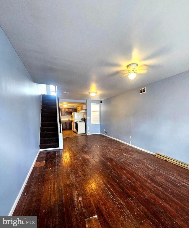 unfurnished living room featuring dark wood-type flooring and ceiling fan