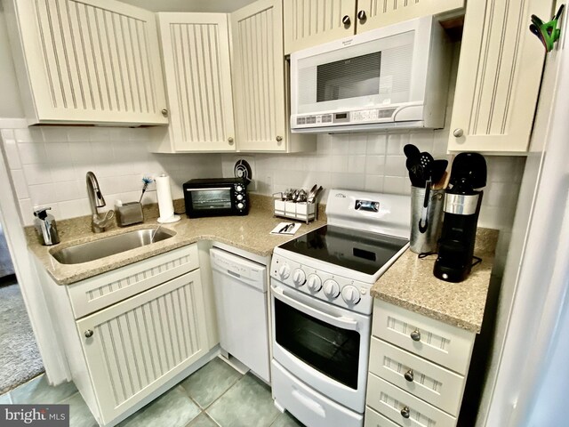 kitchen with light tile patterned floors, white appliances, light stone countertops, a sink, and backsplash