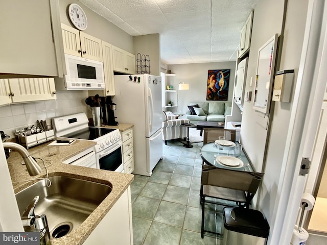 kitchen featuring white appliances, light stone counters, a sink, open floor plan, and decorative backsplash