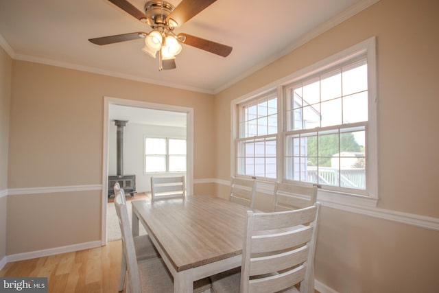 unfurnished dining area featuring ceiling fan, light wood-type flooring, crown molding, and a wood stove