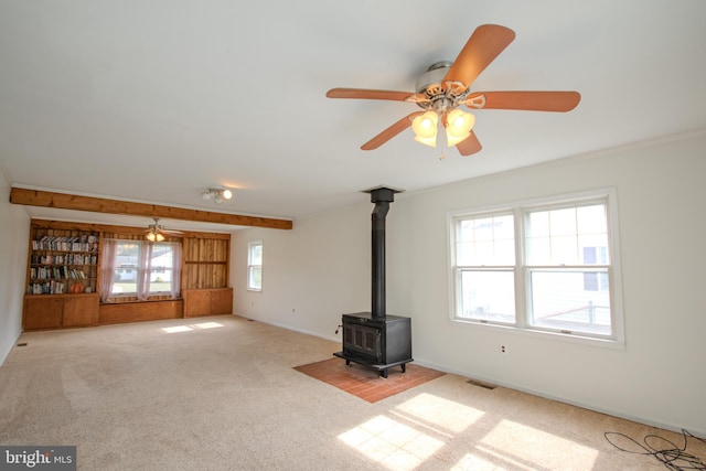 unfurnished living room with light colored carpet, plenty of natural light, and a wood stove