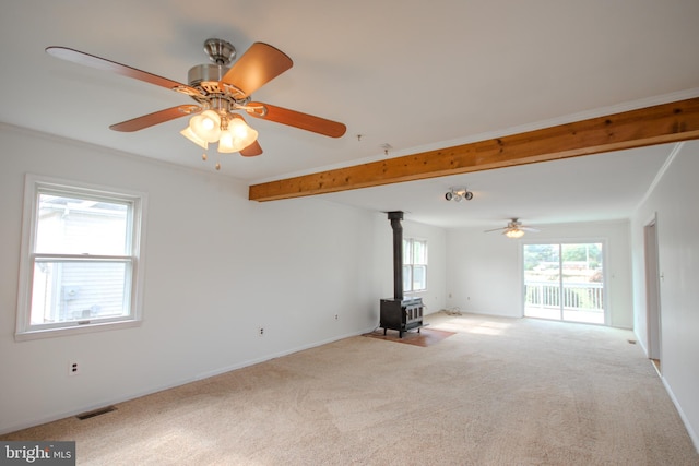 unfurnished living room featuring ceiling fan, a healthy amount of sunlight, light colored carpet, and a wood stove