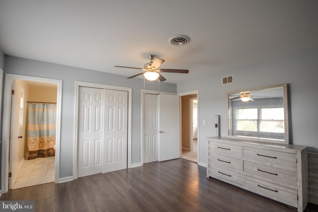 bedroom with ceiling fan, two closets, ensuite bath, and dark wood-type flooring