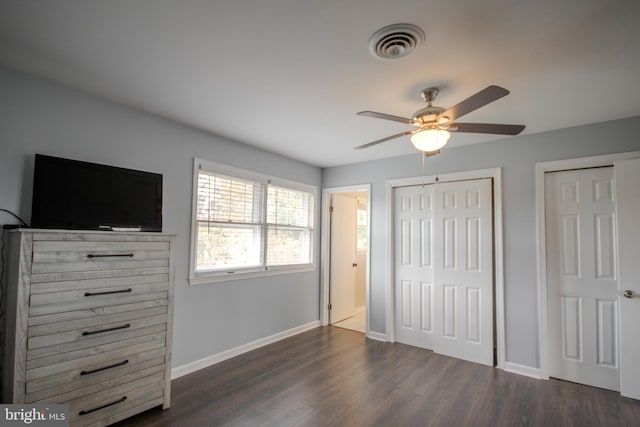 unfurnished bedroom featuring ceiling fan, multiple closets, and dark hardwood / wood-style flooring