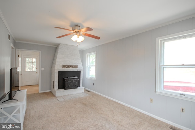 unfurnished living room with ceiling fan, light colored carpet, crown molding, and a wood stove