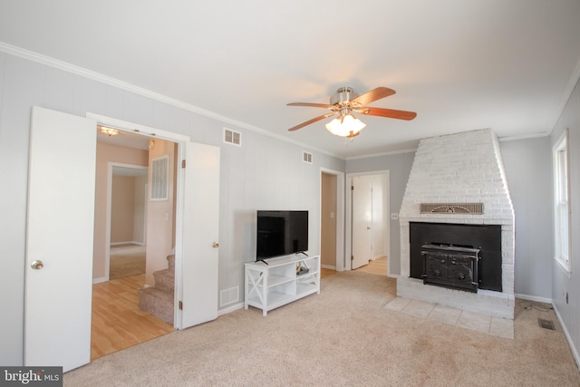 unfurnished living room with ornamental molding, light carpet, a wood stove, and ceiling fan