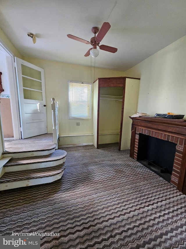 interior space with ceiling fan, lofted ceiling, a brick fireplace, and dark carpet