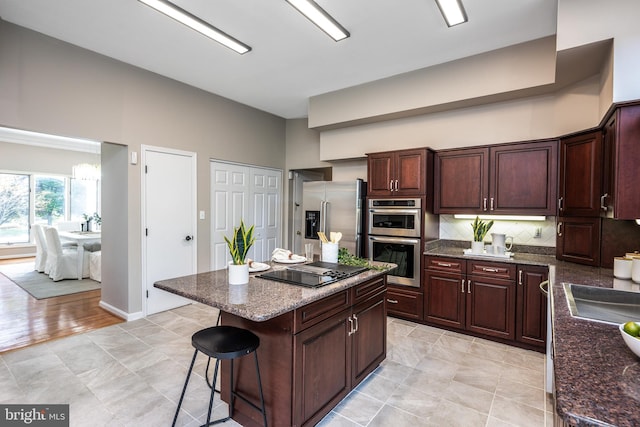 kitchen with appliances with stainless steel finishes, a kitchen bar, a kitchen island, backsplash, and dark brown cabinets