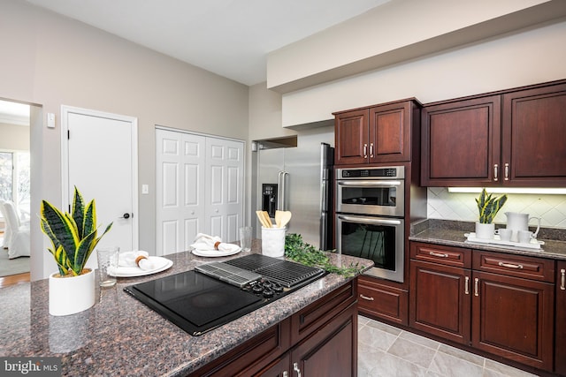 kitchen with decorative backsplash, appliances with stainless steel finishes, light tile patterned floors, and dark stone counters